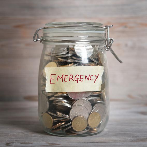 Coins in glass money jar with emergency label, financial concept. Vintage wooden background with dramatic light.