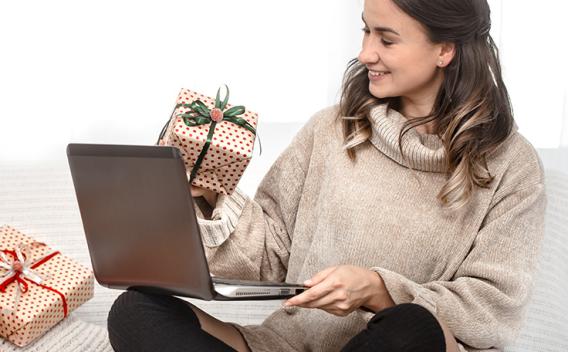 A woman sitting on the floor with a laptop and wrapped presents beside her