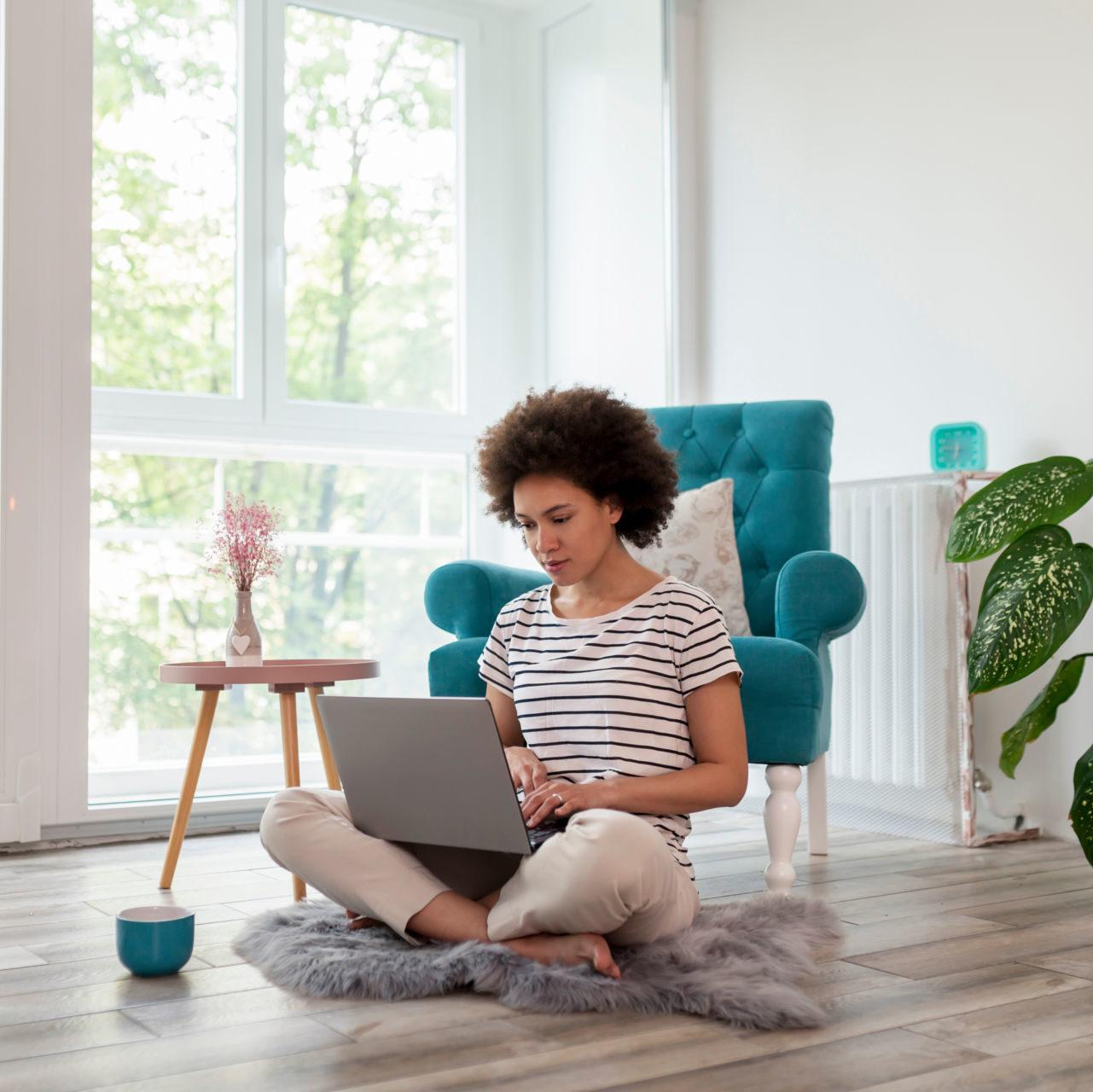 A young woman sitting on a living room floor using a laptop