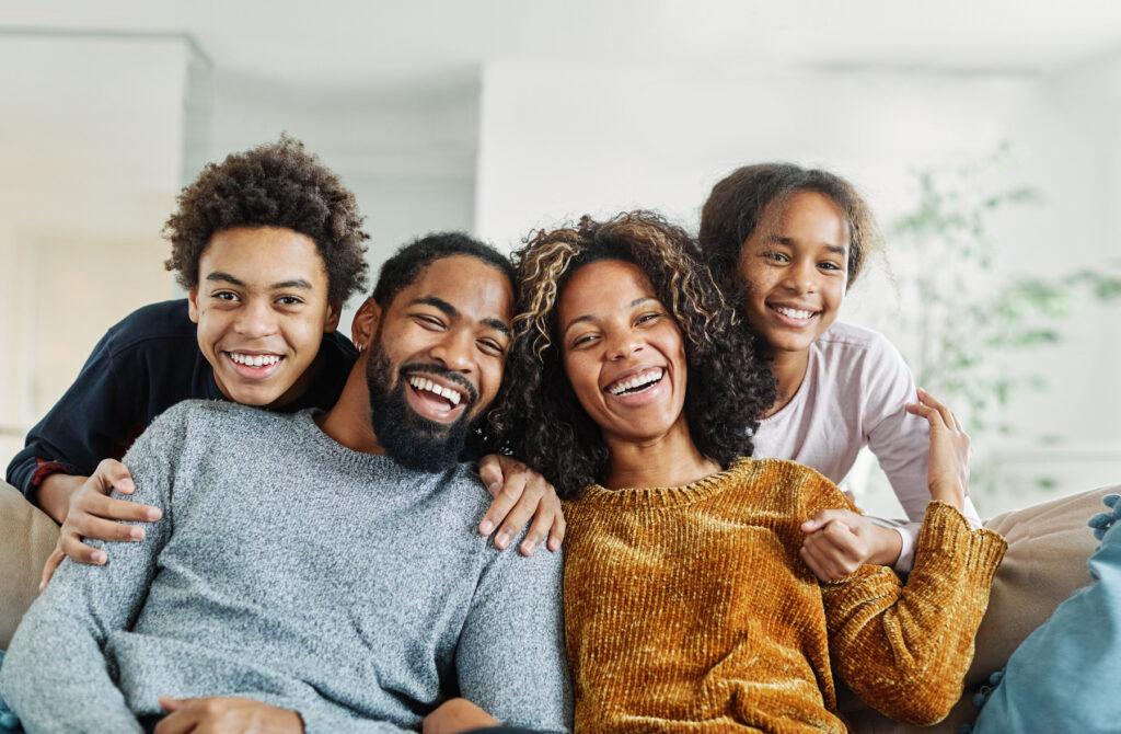 A family of four is sitting on a couch smiling