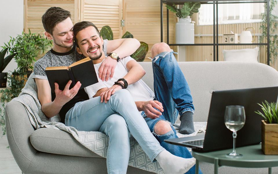 Two men holding each other on a couch while looking at a book