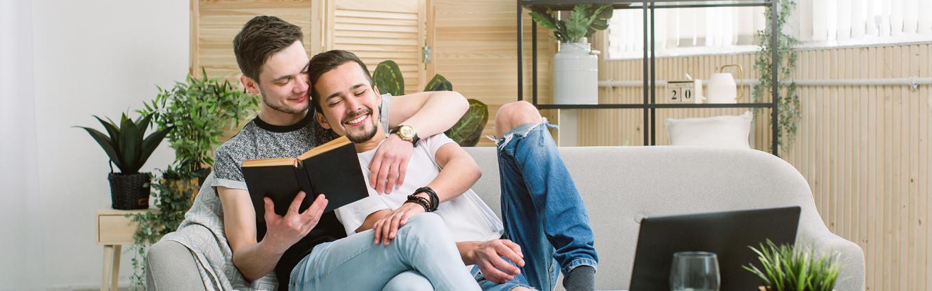 Two men holding each other on a couch while looking at a book