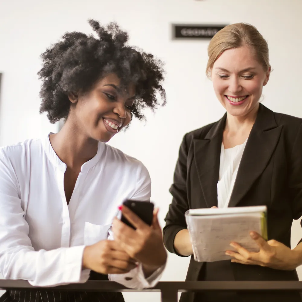 Two professionals looking at data on a phone and notebook