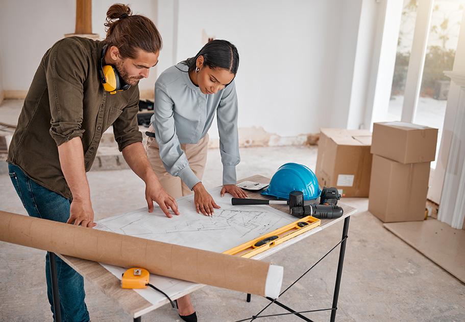 Two professionals review architectural blueprints on a table at a renovation site, surrounded by construction tools and boxes.