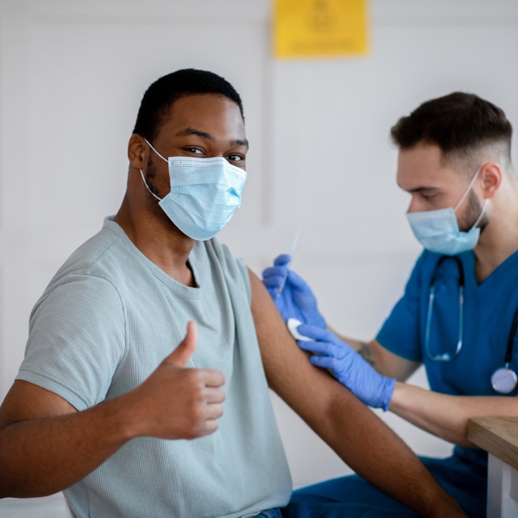 African american man in mask gesturing thumb up during coronavirus vacination