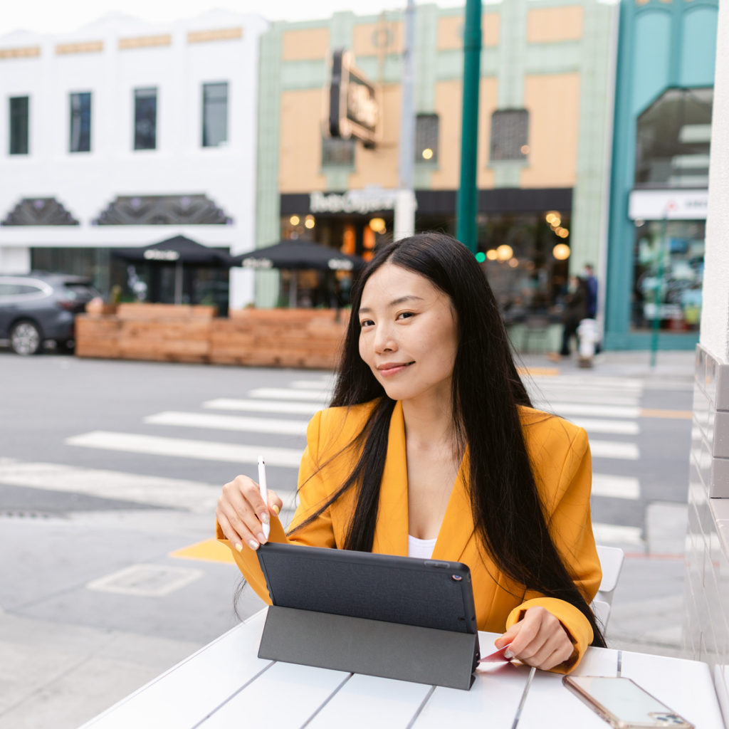 A young woman considers debt management plan pros and cons while sitting with a laptop at an outdoor cafe